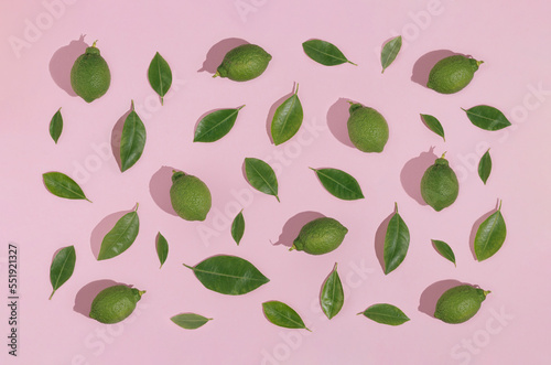 Creative pattern made of green lemons, limes and green leaves on pastel pink background. Fruit minimal concept. Flat lay.