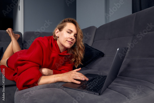 Very tired young woman, burning the midnigh oil - working late at night on her laptop computer, at home, sitting on sofa, rubbing her tired eyes, trying to stay focused. photo