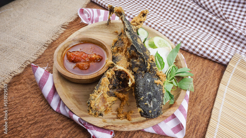 Fried catfish or “Pecel Lele” with fresh raw vegetables served on wooden plate. Indonesian food with fried catfish and fresh vegetables and sambal. photo