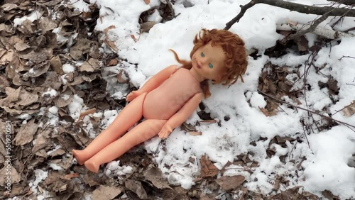 Abandoned baby naked doll lies on the snow among the rotten leaves on a winter day photo