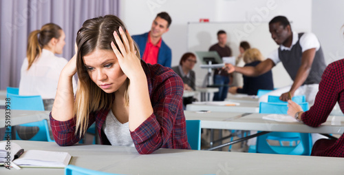 Portrait of frustrated young woman student sitting separately in classroom in break between lessons