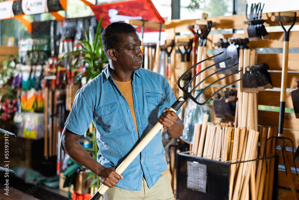 Focused adult african american man looking for pitchfork to work in his garden at gardening supply store