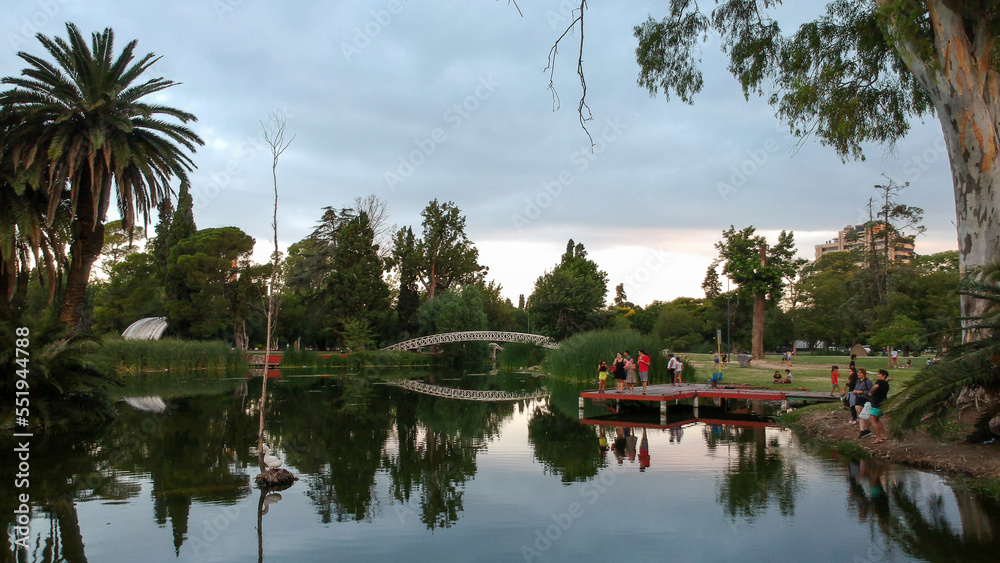 Lago con un puente rodeado de palmeras y arboles con gente y reflejo del agua