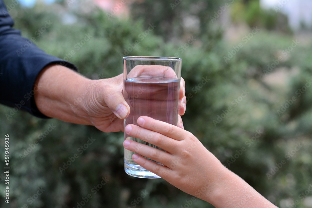 Child giving glass of water to elderly woman outdoors, closeup Child giving glass of water to elderly woman outdoors, closeup