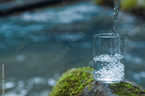 Fresh water pouring into glass on stone near river. Space for text © New Africa