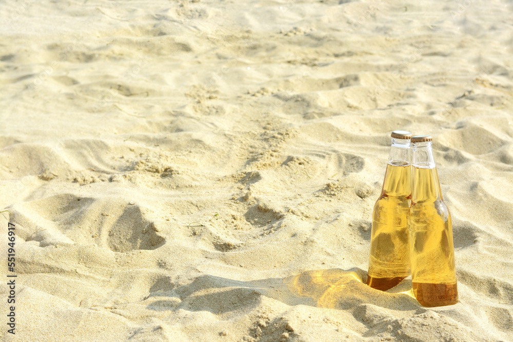 Bottles of cold beer on sandy beach near sea, space for text Bottles of cold beer on sandy beach near sea, space for text