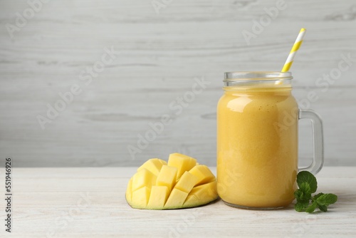 Mason jar with delicious fruit smoothie and fresh mango on white wooden table. Space for text