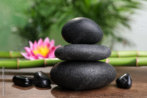 Stacked spa stones, bamboo stems and flower on wooden table against blurred background