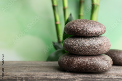Stacked spa stones on wooden table against bamboo stems and green leaves. Space for text