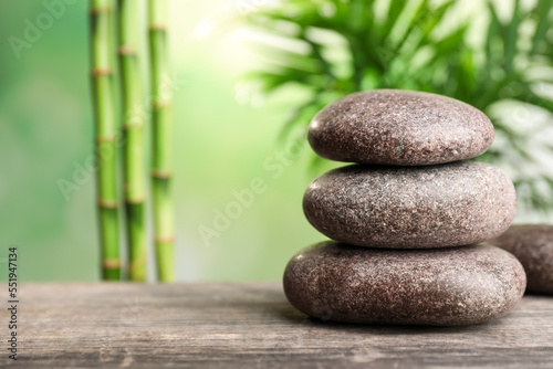 Stacked spa stones on wooden table against bamboo stems and green leaves. Space for text