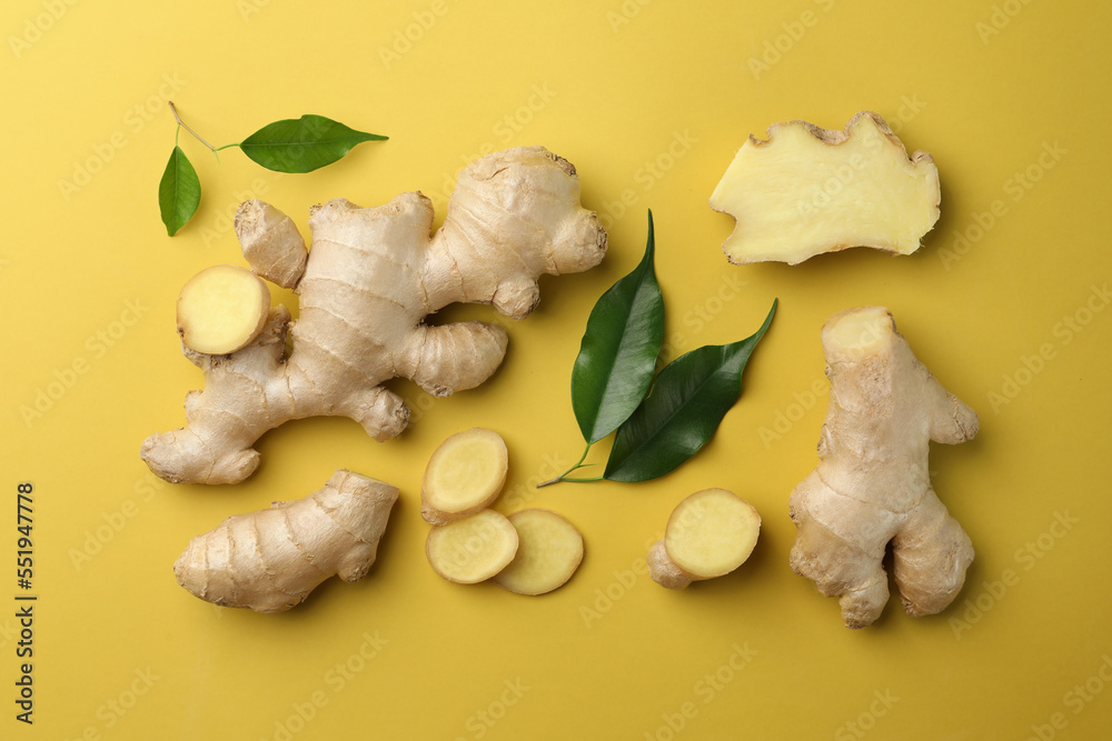 Fototapeta premium Fresh ginger with green leaves on pale light yellow background, flat lay
