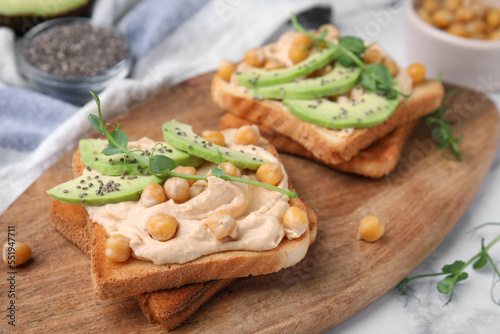 Delicious sandwiches with hummus, avocado and chickpeas on wooden board