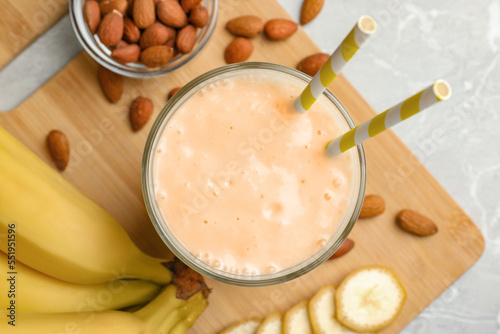 Flat lay composition of banana smoothie in glass and nuts on light grey table