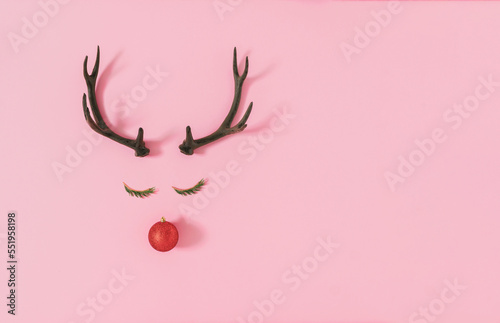 Trendy Christmas composition made of evergreen for, red bauble decoration and antlers on pastel pink background. Creative art minimal aesthetics..Minimal winter holidays idea. Flat lay, top view