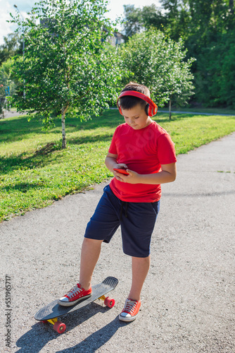 Chubby ten years old boy spends free time training skating in the city park. Boy looking on mobile phone.