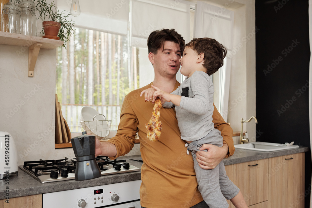 Mature man with coffee pot holding his little son chatting with him in kitchen horizontal medium shot Mature man with coffee pot holding his little son chatting with him in kitchen horizontal medium shot
