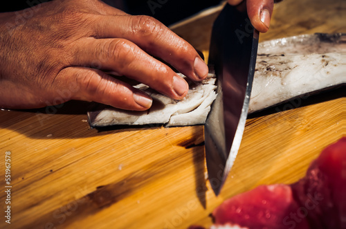 Close up of Chef cook hands chopping Saba fish for traditional Asian cuisine with Japanese knife. Professional Sushi chef cutting seafood japanese chefs are making Saba fish sashimi. Dark Tone