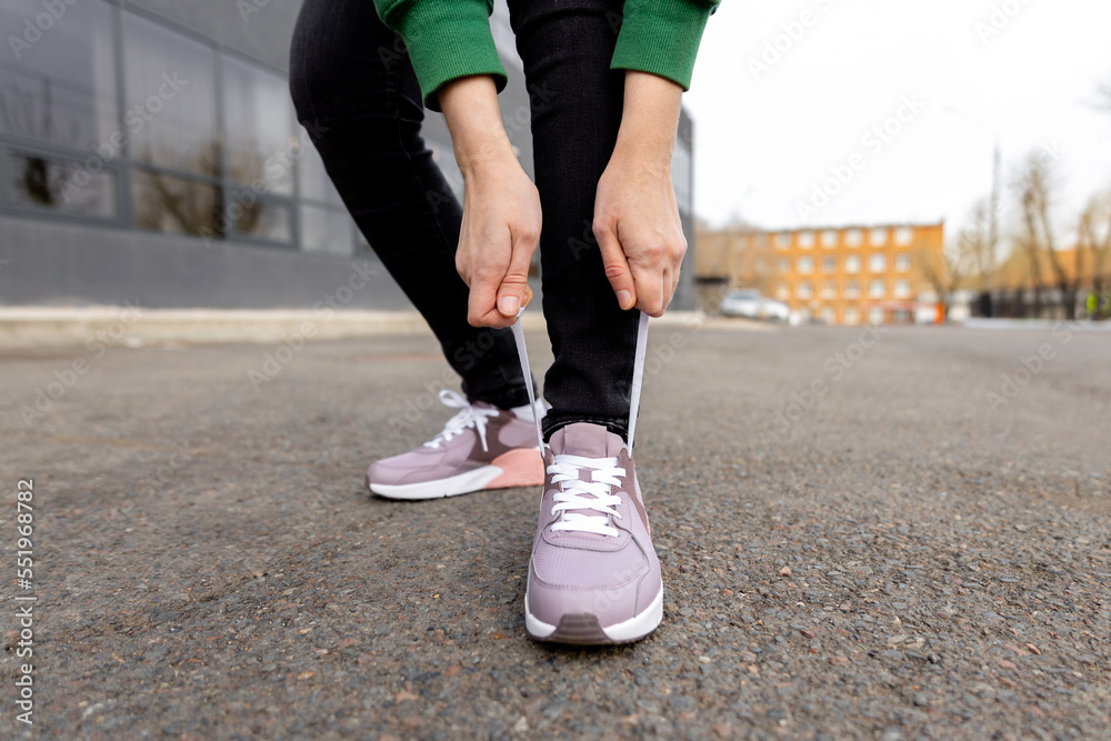 woman stands on an asphalt road and ties her shoelaces. Womans legs in pink sneakers close up