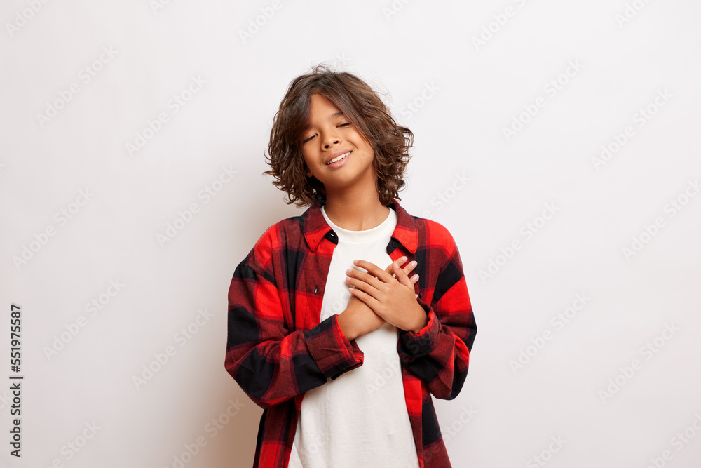 Attractive dark skinned teenager put hands over heart, smile toothily, isolated over white background Attractive dark skinned teenager put hands over heart, smile toothily, isolated over white background