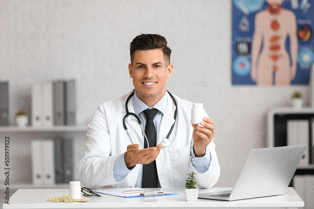 Male doctor with bottle of vitamin A sitting at table in clinic Male doctor with bottle of vitamin A sitting at table in clinic