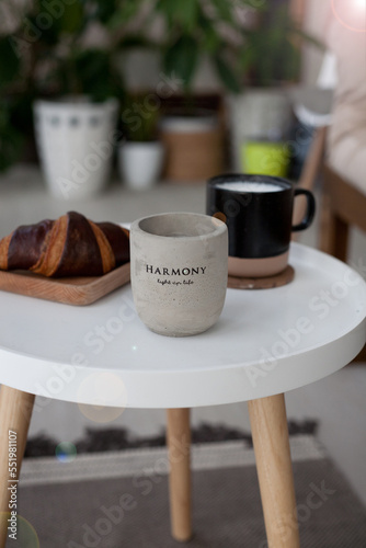 white round table with ceramic concrete candles, coffee, croissant and magazine, cozy interior