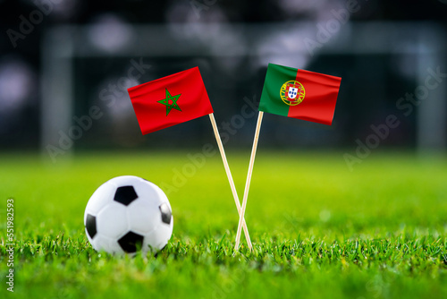 Morocco - Portugal. Quarter-finals football match. Round of 8. Handmade national flags and soccer ball on green grass. Football stadium in background. Black edit space.