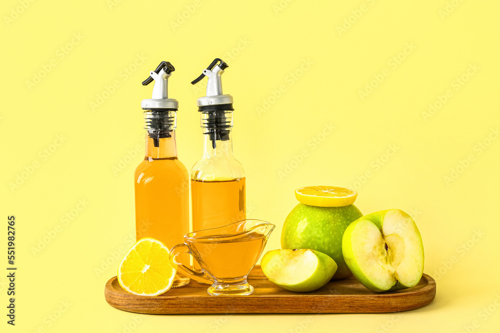 Wooden board with bottles of apple cider vinegar and fruits on yellow background Wooden board with bottles of apple cider vinegar and fruits on yellow background
