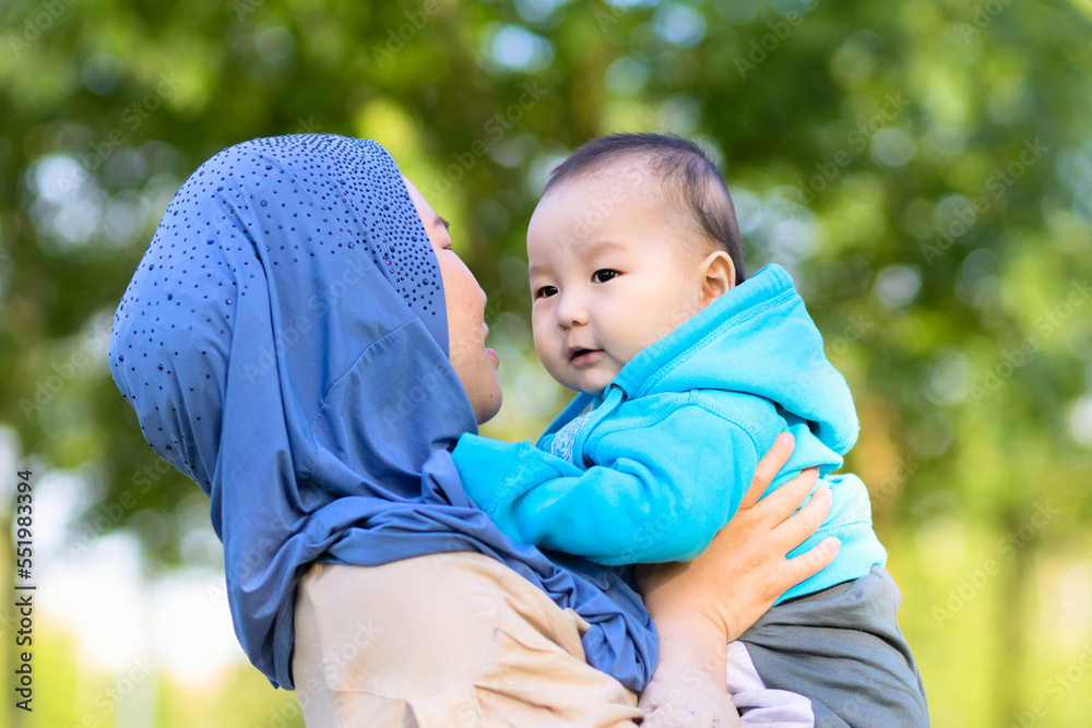 Cute young islamic kazakh woman hugging, playing with her little son, newborn boy. happy asian mother in hijab holding baby in hands outdoors. Family concept Cute young islamic kazakh woman hugging, playing with her little son, newborn boy. happy asian mother in hijab holding baby in hands outdoors. Family concept