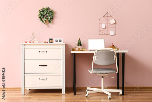 Workplace with laptop and Christmas gifts near pink wall in office