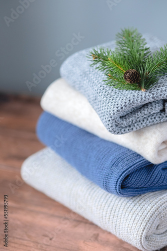 A stack knitted clothes decorated with a Christmas tree branch with a cone on a gray background. Change of season and wardrobe. Sustainable and ecological fashion.