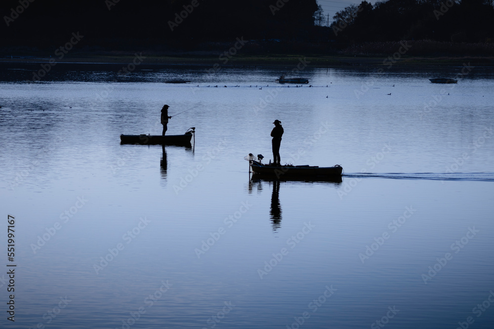 静かな水面で行き交う釣り人のシルエット