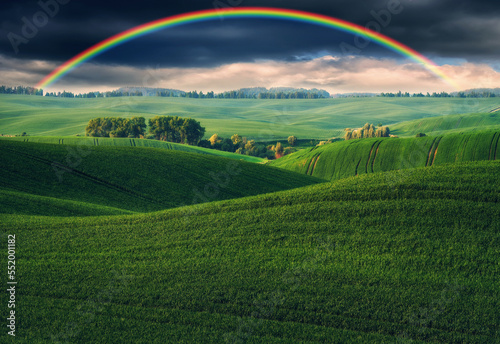 Scenic view of rainbow over green field. dramatic gray sky over a picturesque hilly field© sergnester