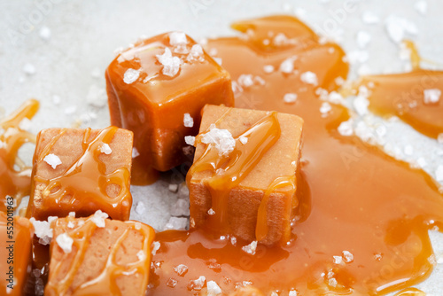 Salted caramel, a taste sensation. Coarse salt and caramel blocks covered in a sticky creamy salted caramel sauce on grey photo