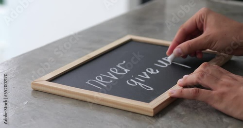 female hands drawing with chalk on a blackboard motivational phrase never give up. Business concept photo