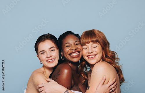 Group of happy women with different skin tones smiling and embracing each other in a studio
