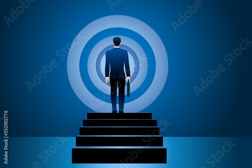 Back view of businessman with suitcase standing near target figure on black wall, concept of achieving goal successful business.