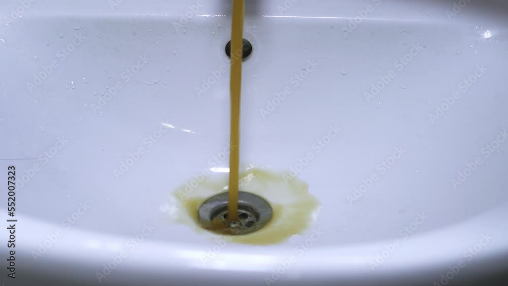 Dirty rusty water flows from the tap. Yellow and brown tap water flows