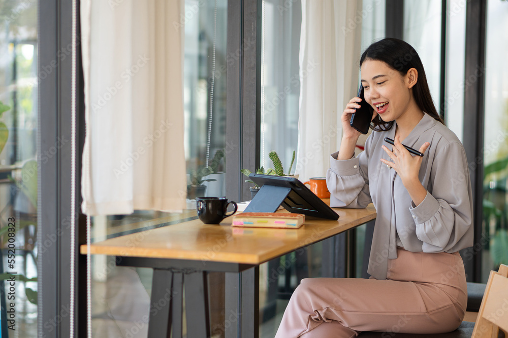 Pretty asian professional businesswoman holding smartphone to talk, chat and save data on tablet happily while in coffee shop, online working concept Pretty asian professional businesswoman holding smartphone to talk, chat and save data on tablet happily while in coffee shop, online working concept