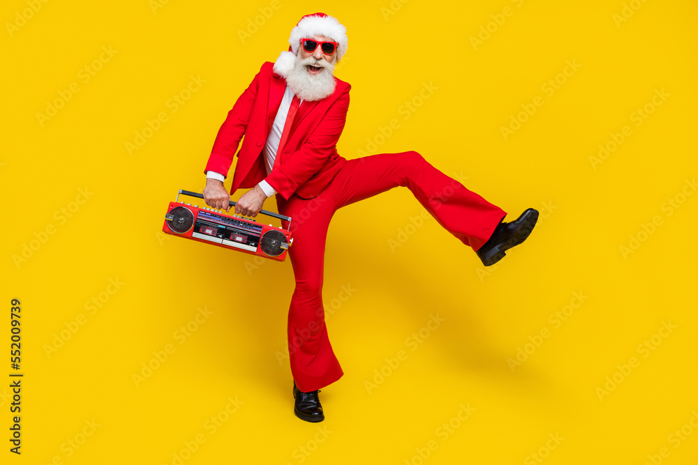Full length photo of funny positive retired guy wear red tux claus hat dancing enjoying boom box isolated yellow color background Full length photo of funny positive retired guy wear red tux claus hat dancing enjoying boom box isolated yellow color background