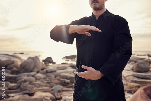 Health, fitness and tai chi with a man using martial arts for spiritual wellness and exercise by the beach. Fit, strong and asian zen lifestyle with chi gong by the seaside and a male active person