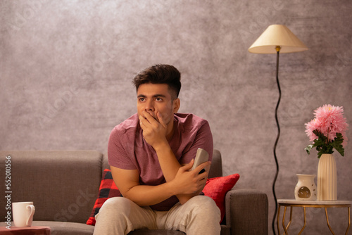 Young man watching TV while sitting on sofa in living room