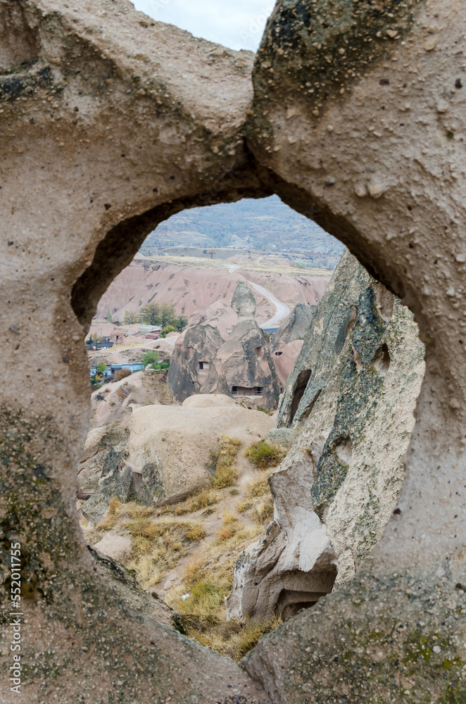 The view through hole eroded in cave of Uchisar town volcanic rocks in autumn day on other caves, rocks and valley in Cappadocia region, Turkey