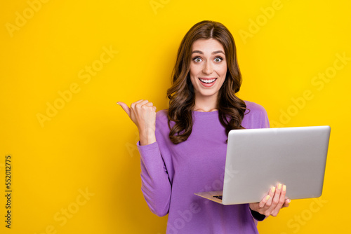 Portrait of excited cheerful girl hold netbook indicate thumb finger empty space isolated on yellow color background