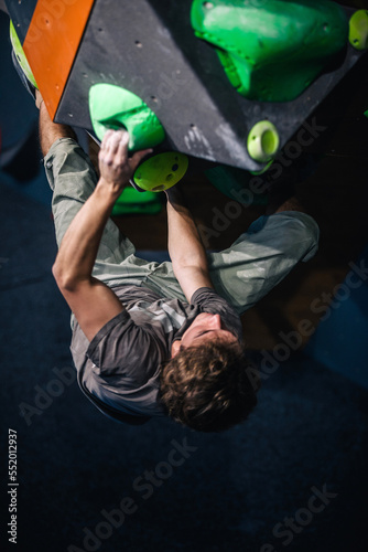 A young, athletic guy with a beautiful inflated body climbs a bouldering in a climbing hall. Emotions on the face.