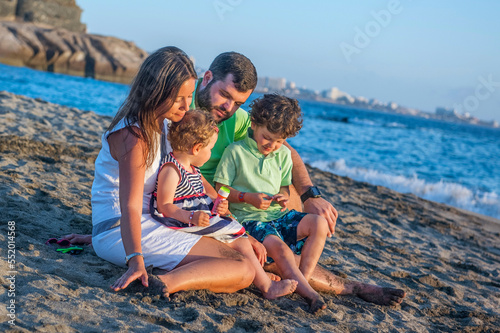 Family: dad, mom, little daughter and little son sitting on the beach by the ocean