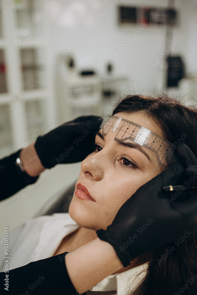 Fototapeta premium Woman in gloves making measuring of the brows with a ruler before permanent makeup procedure. Closeup shot