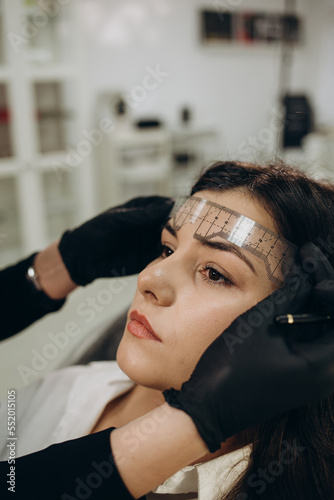 Woman in gloves making measuring of the brows with a ruler before permanent makeup procedure. Closeup shot