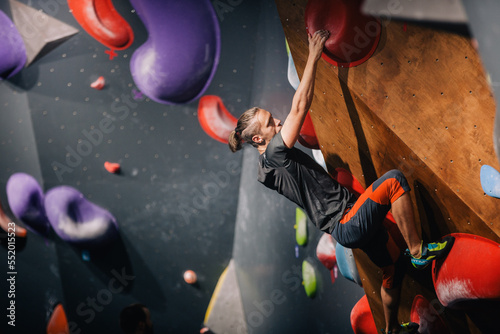 A young, athletic guy with a beautiful inflated body climbs a bouldering in a climbing hall. Emotions on the face.