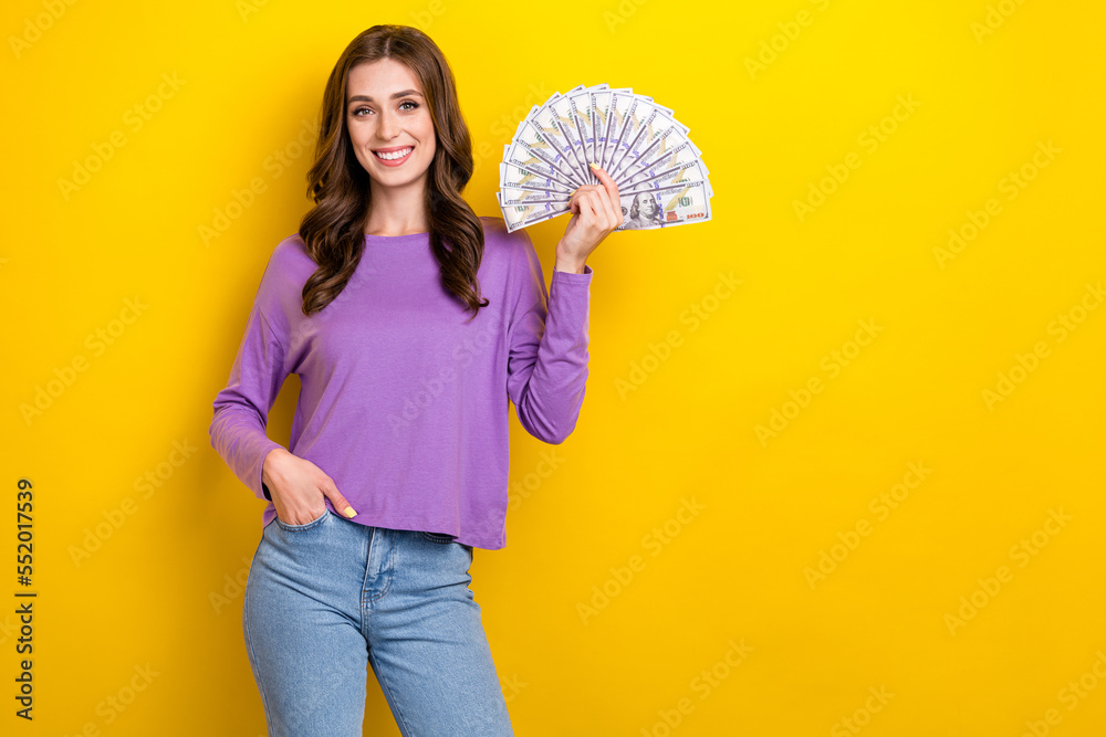Photo of funny cheerful girl dressed purple pullover holding dollars fan empty space isolated yellow color background Photo of funny cheerful girl dressed purple pullover holding dollars fan empty space isolated yellow color background