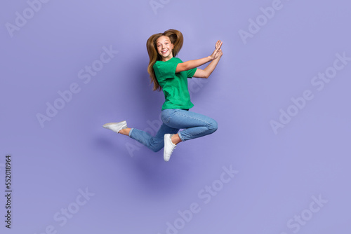 Full length photo of excited shiny girl dressed green t-shirt smiling jumping high isolated purple color background